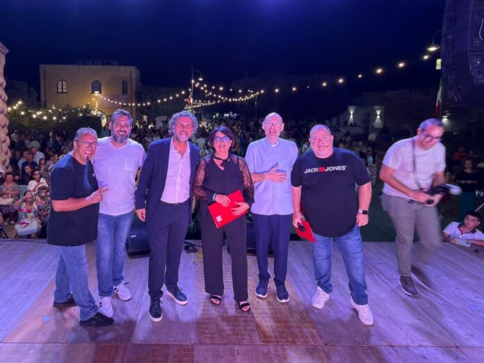 Foto di gruppo sul palco della Sagra dell’Uva e del Vino a Petrosino, con il pubblico sullo sfondo